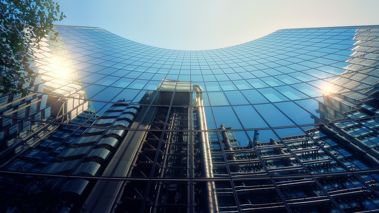 A picture looking up at the front of a skyscraper in the City of London. The mirrored front reflecting other buildings opposite, one of which is the headquarters of Lloyd's of London.