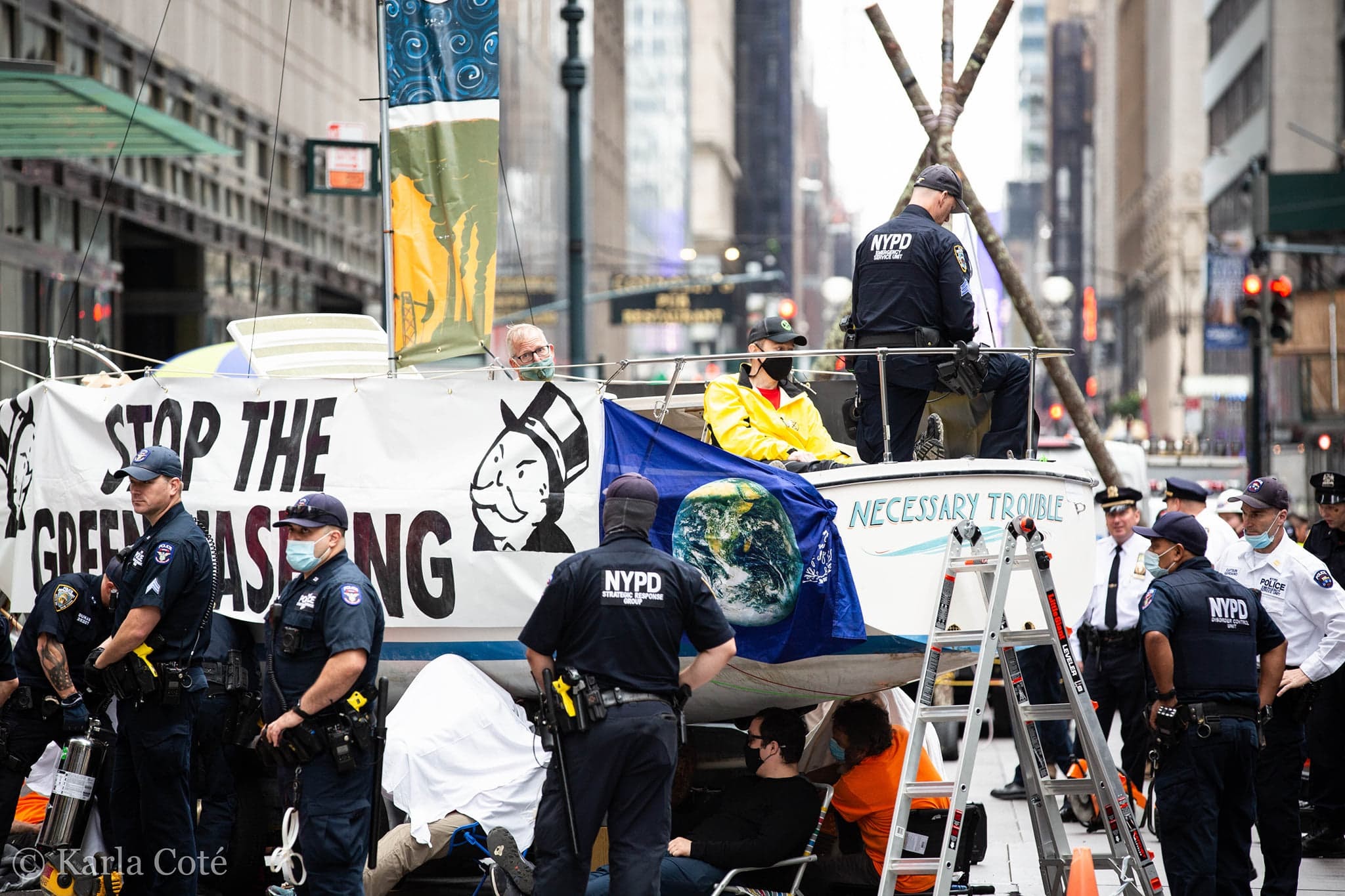 Police struggle to remove rebels chained to a sailboat decked in banners on a main road.