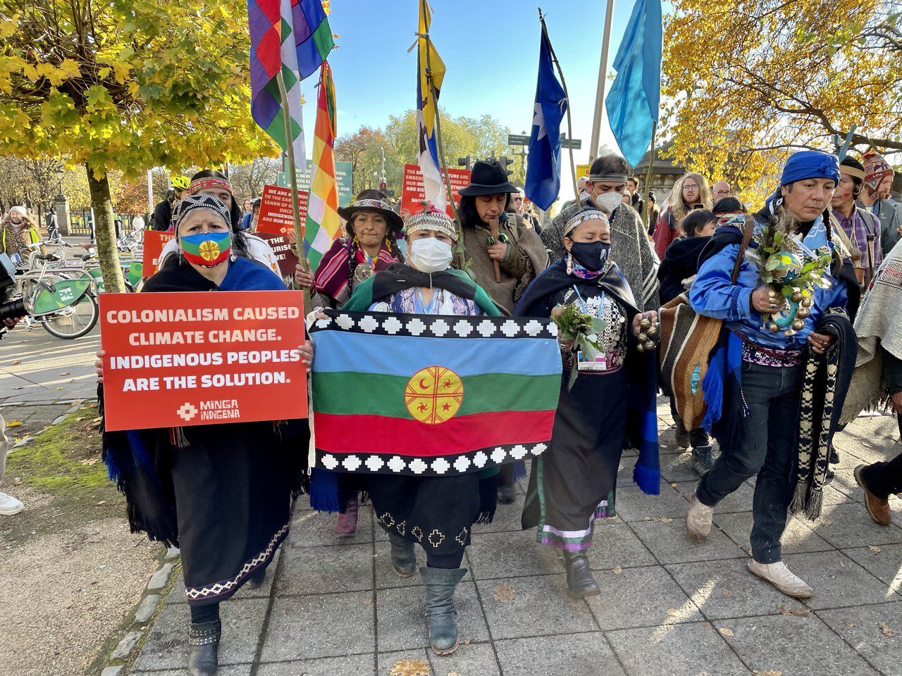 People in colourful tribal dress hold flags, flowers and signs as they march forward with purpose